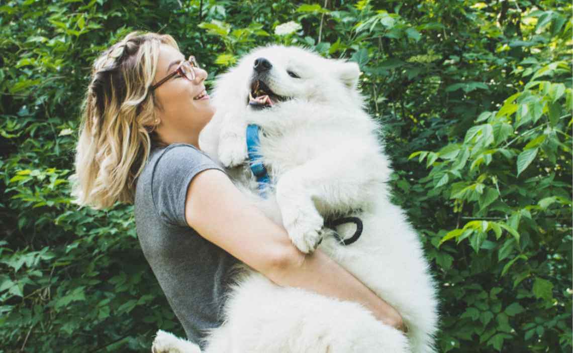 WOMAN HOLDING LARGE WHITE FLUFFY DOG SMILING