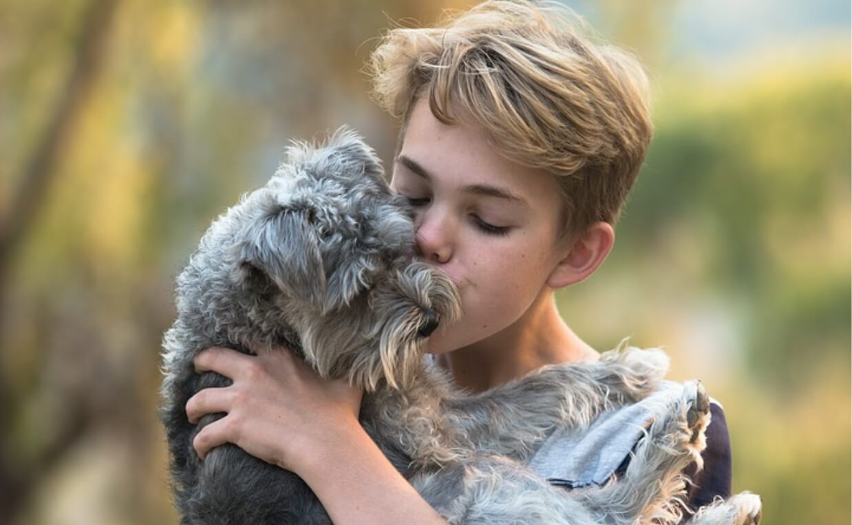 woman with short blonde hair kissing terrier dog