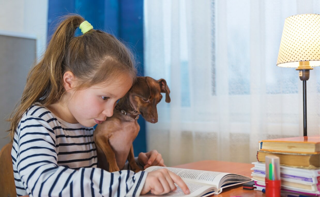 little girl practicing reading with daschund listening