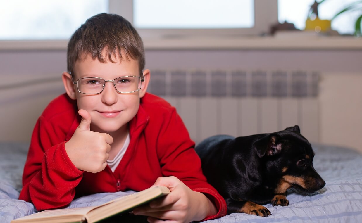 boy gives thumbs up with book in hand and dog by his side