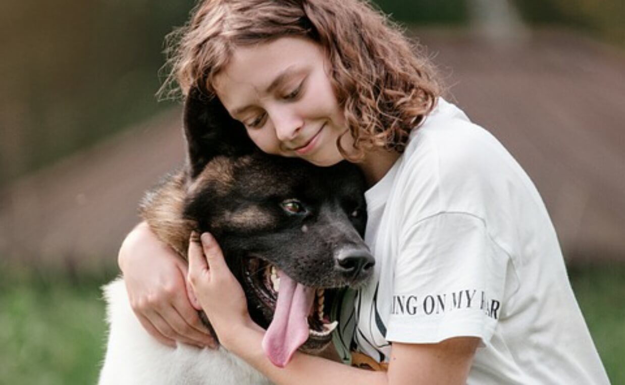 WOMAN HUGGING WHITE BROWN AND BLACK LONG-HAIRED DOG
