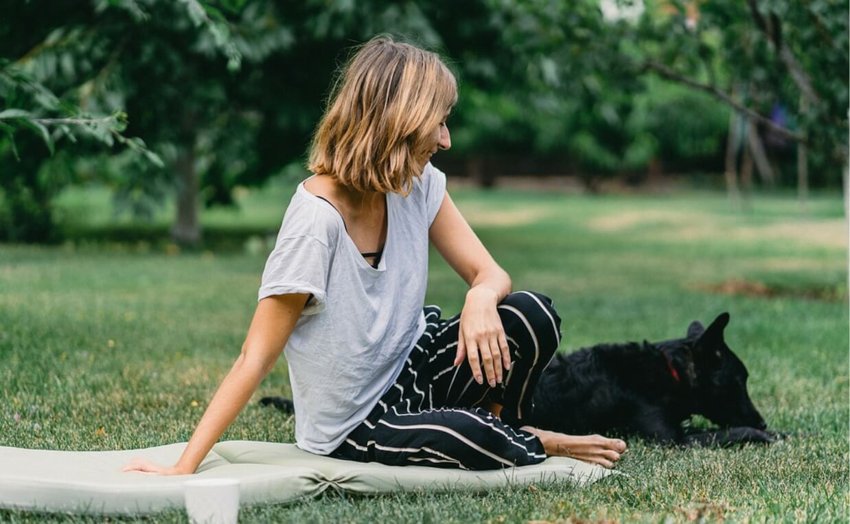 WOMAN ON BLANKET ON LAWN WITH BLACK DOG IN PARK