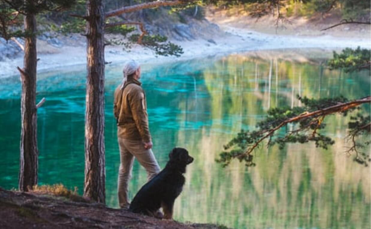man and black dog standing in front of picturesque lake in nature