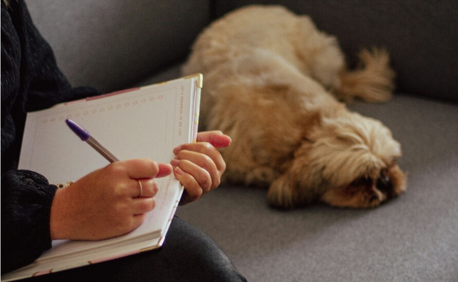 The Unexpected Benefits of a Dog Journal - woman writing in notebook with fluffy tan dog next to her